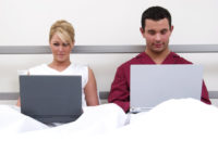 Couple on laptops in bed