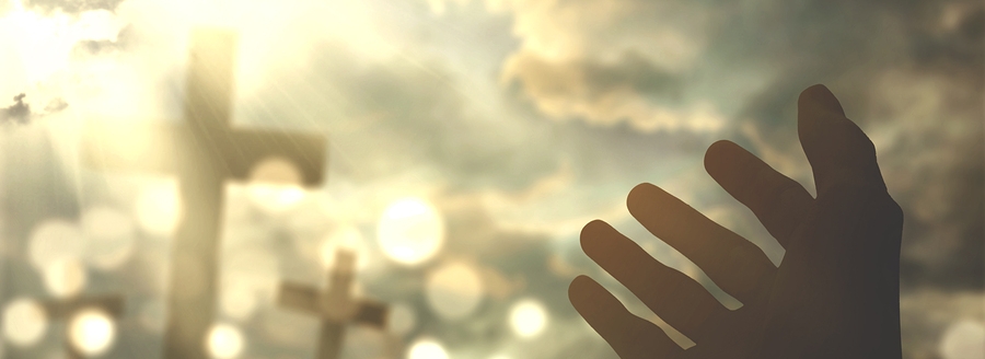 Picture of human hands praying to the GOD with christian cross symbol and bright sunlight on the sky