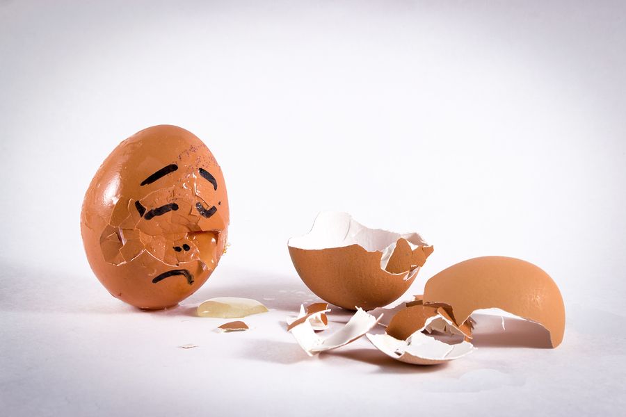 A sad egg with a face cries over the broken egg shells of a friend