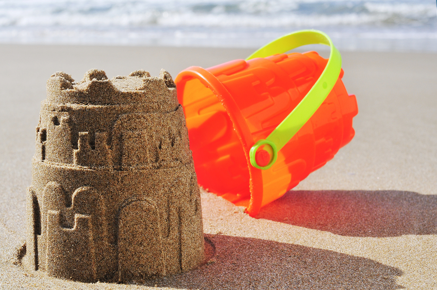 an orange toy bucket and a sandcastle on the sand of a beach an orange toy bucket and a sandcastle on the sand of a beach